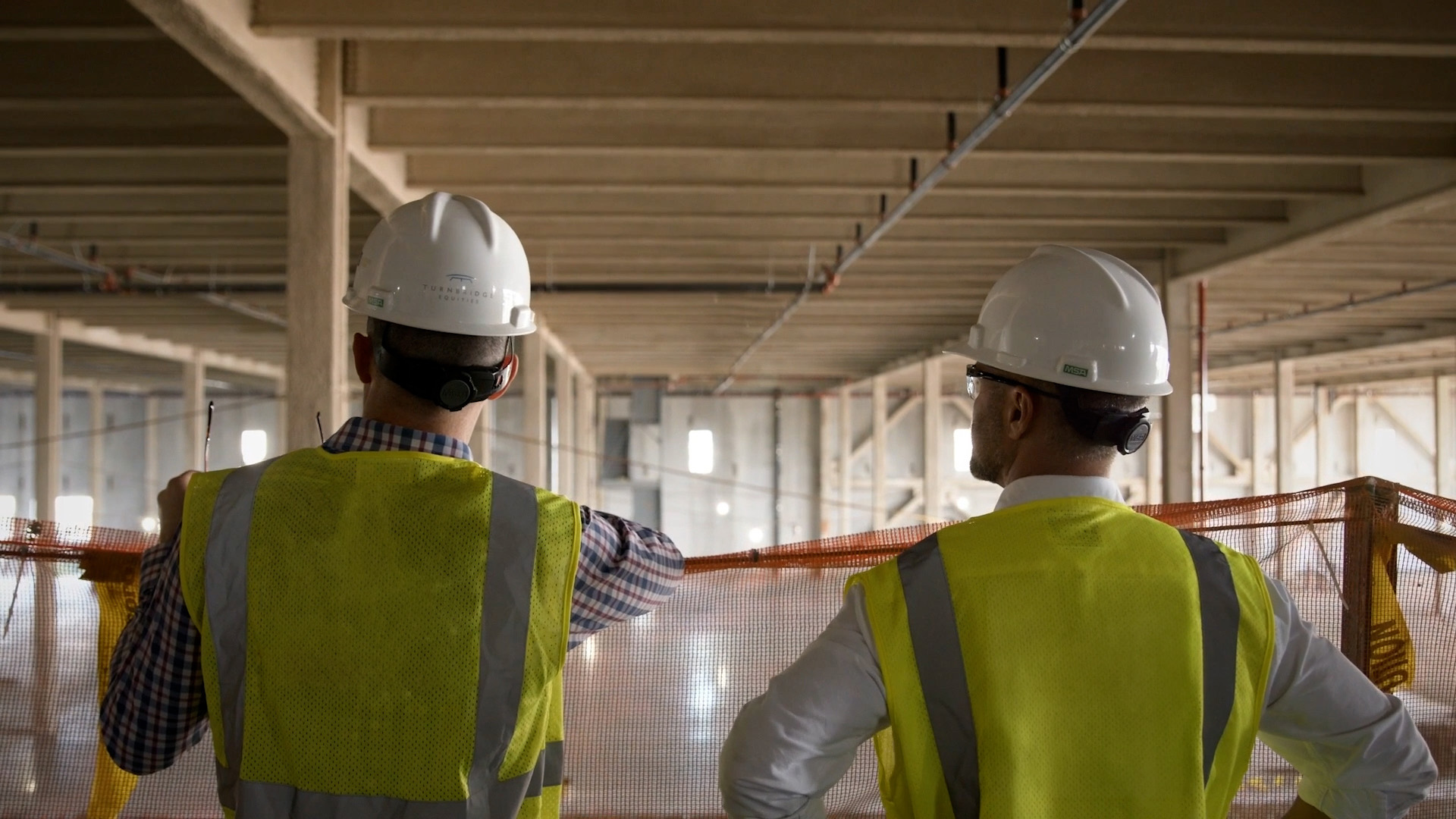 Design team in hard hats and safety vests reviewing an open concrete structure at a construction site.