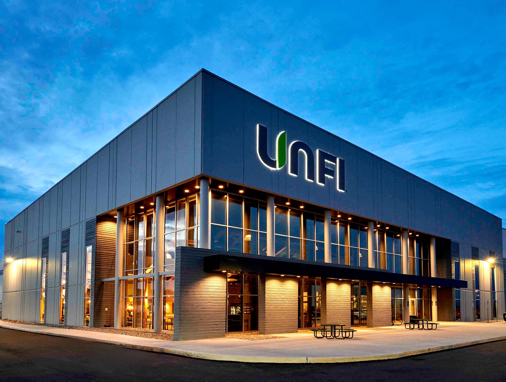 Exterior view of UNFI building with down lighting over entrance and recessed curtain wall.