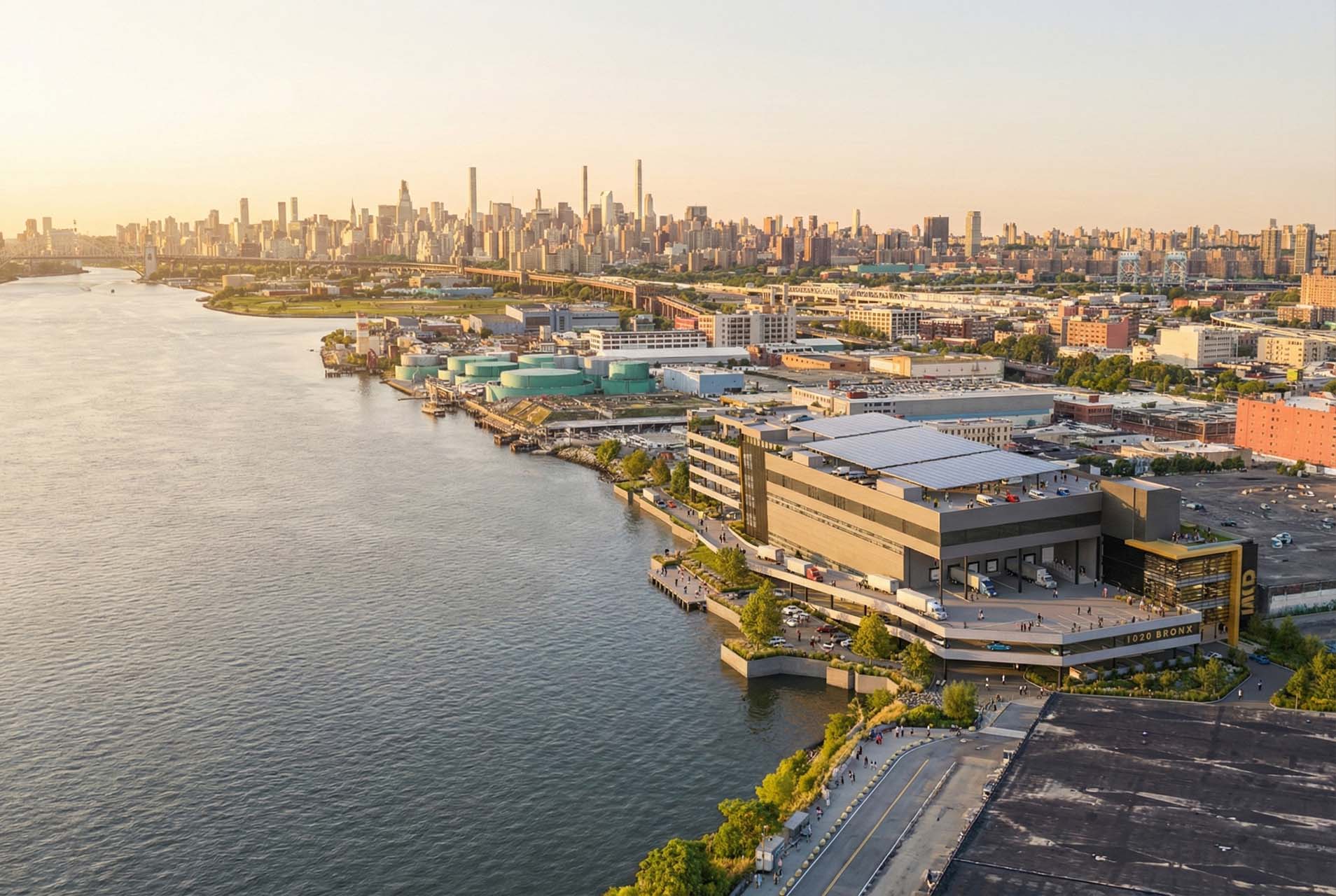 Aerial view of a waterfront industrial building with rooftop solar panels and loading docks, with the Manhattan skyline across the river.