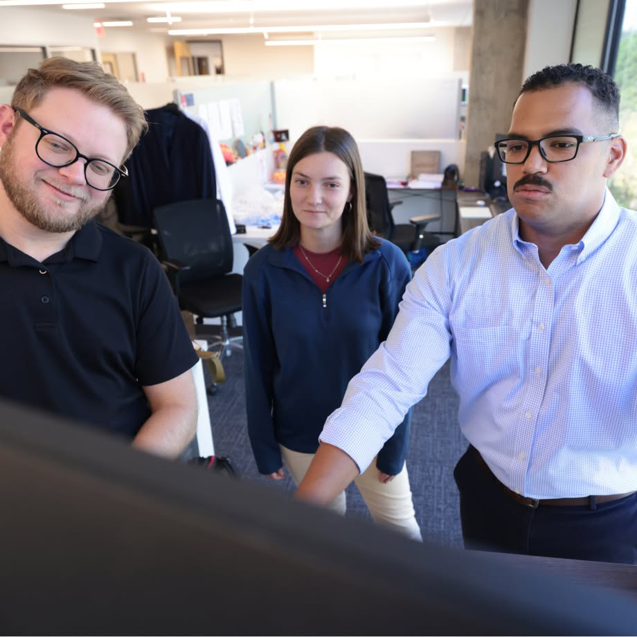 Three colleagues gathered around a computer monitor in an office.