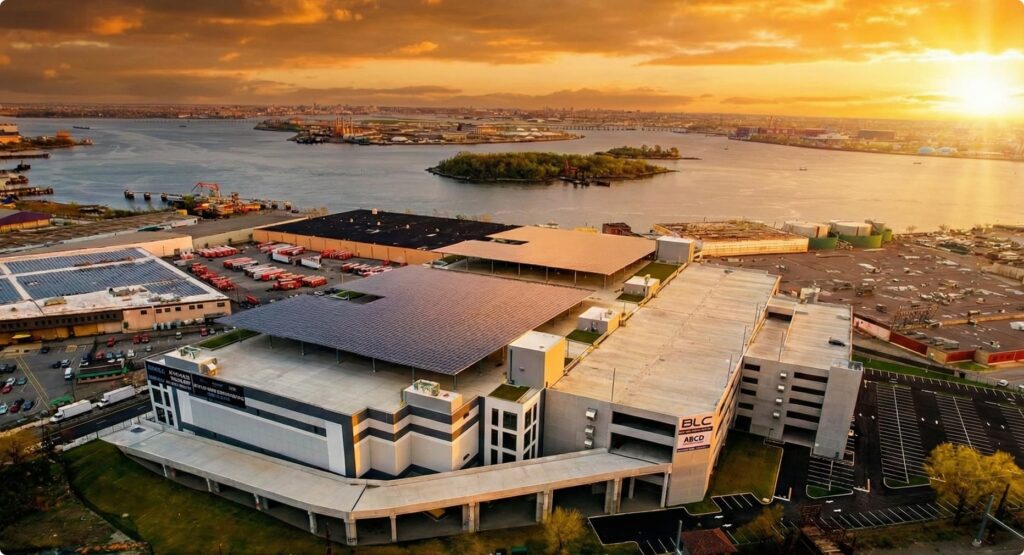 Aerial view of industrial facility by the water with solar panels on roof.