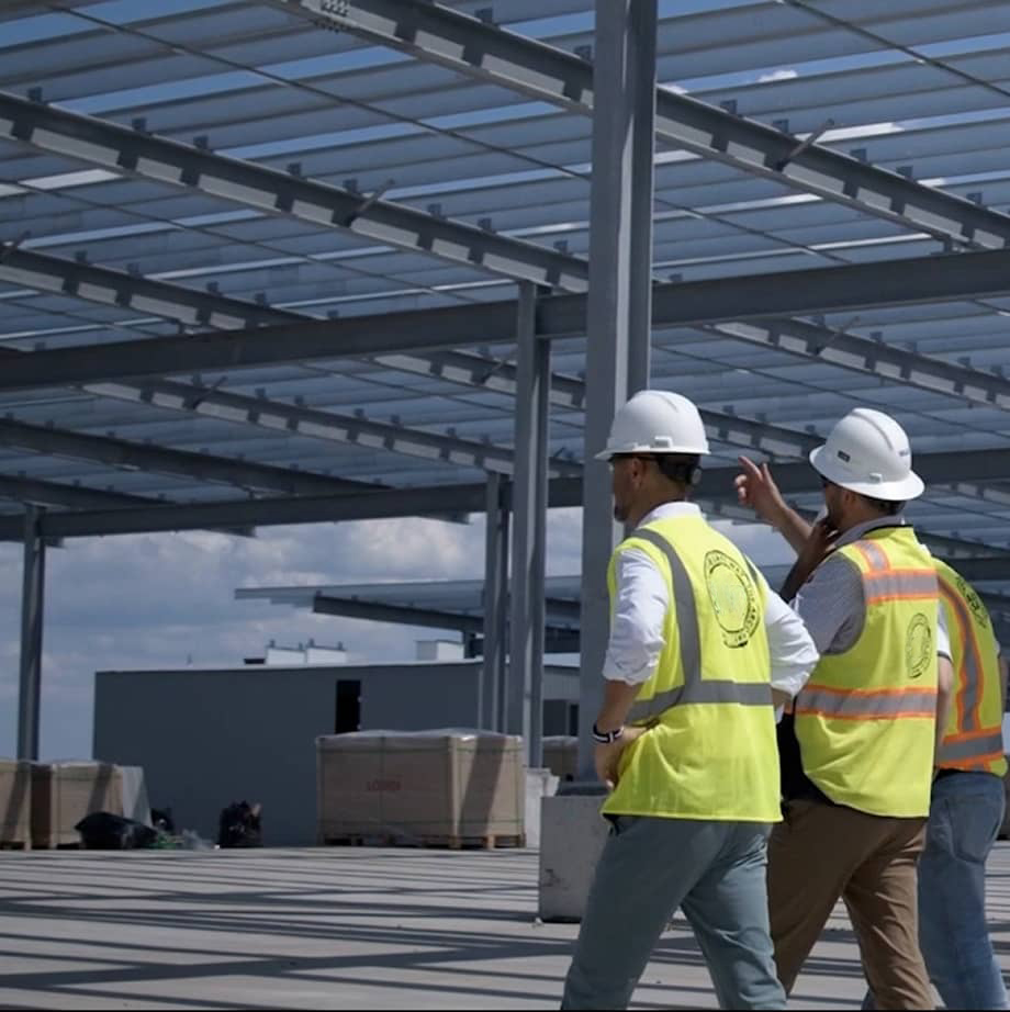 OneFourTwo team in hard hats and safety vests walking through an open steel-framed structure at a construction site.