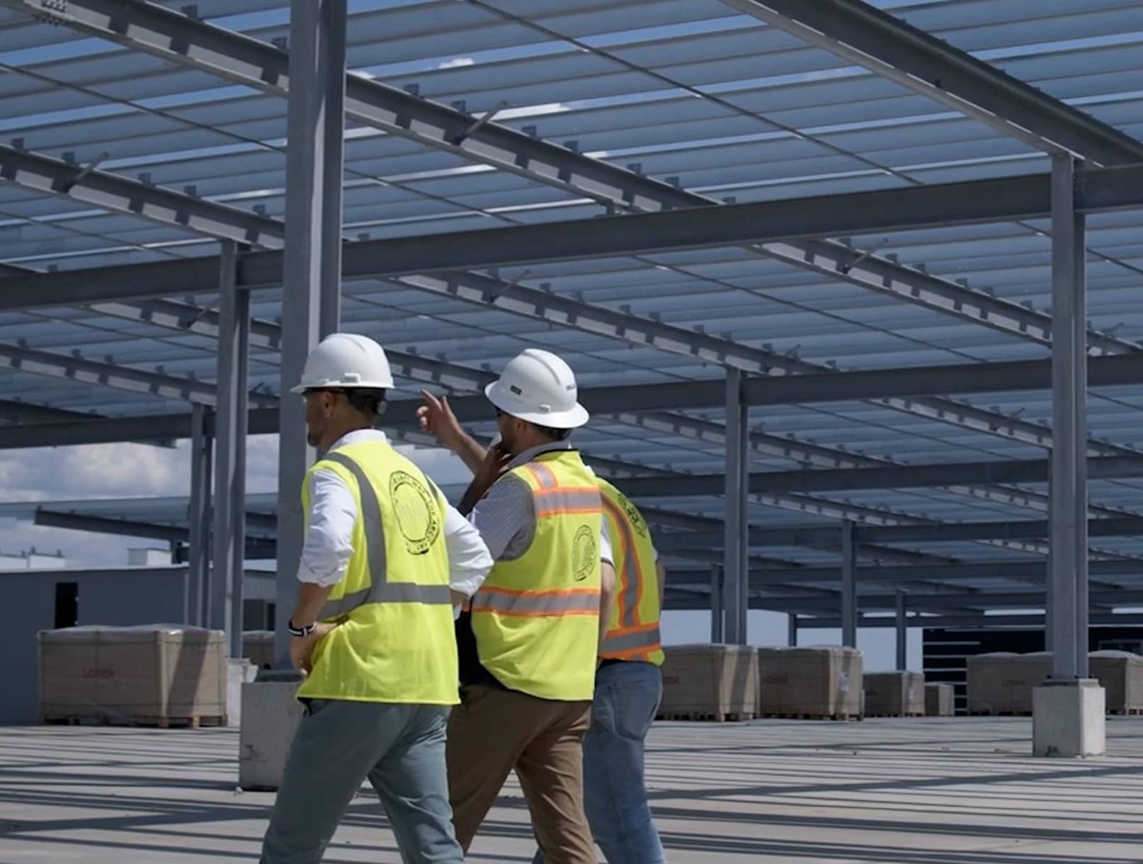 OneFourTwo team in hard hats and safety vests walking through an open steel-framed structure at a construction site.