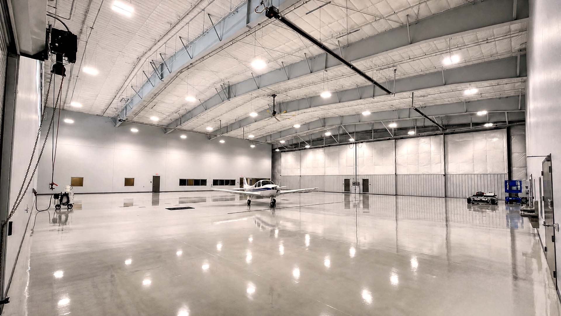 Interior of aircraft hangar with small plane, polished floor, and vaulted metal ceiling.
