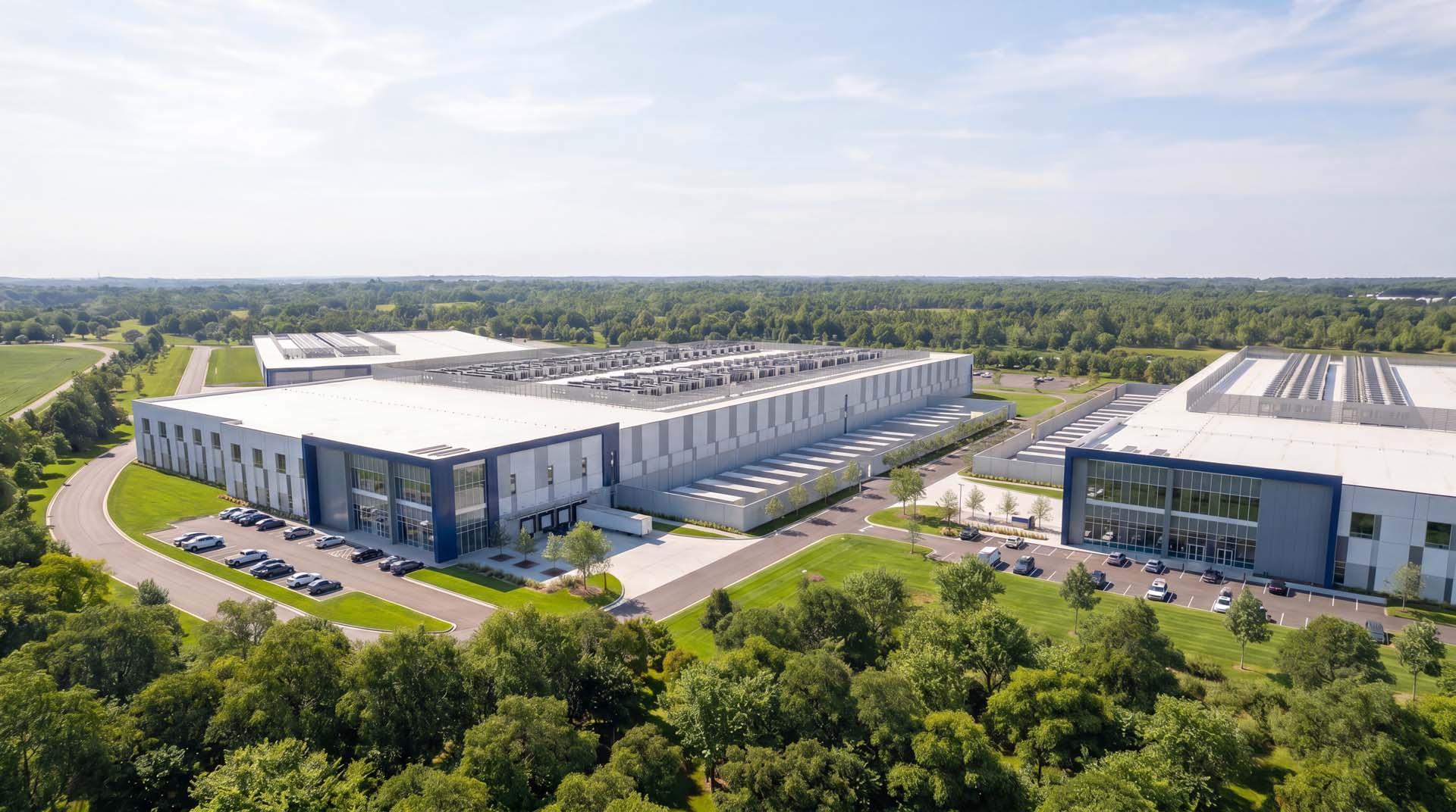 Aerial view of data center building with rooftop cooling units surrounded by trees and parking.