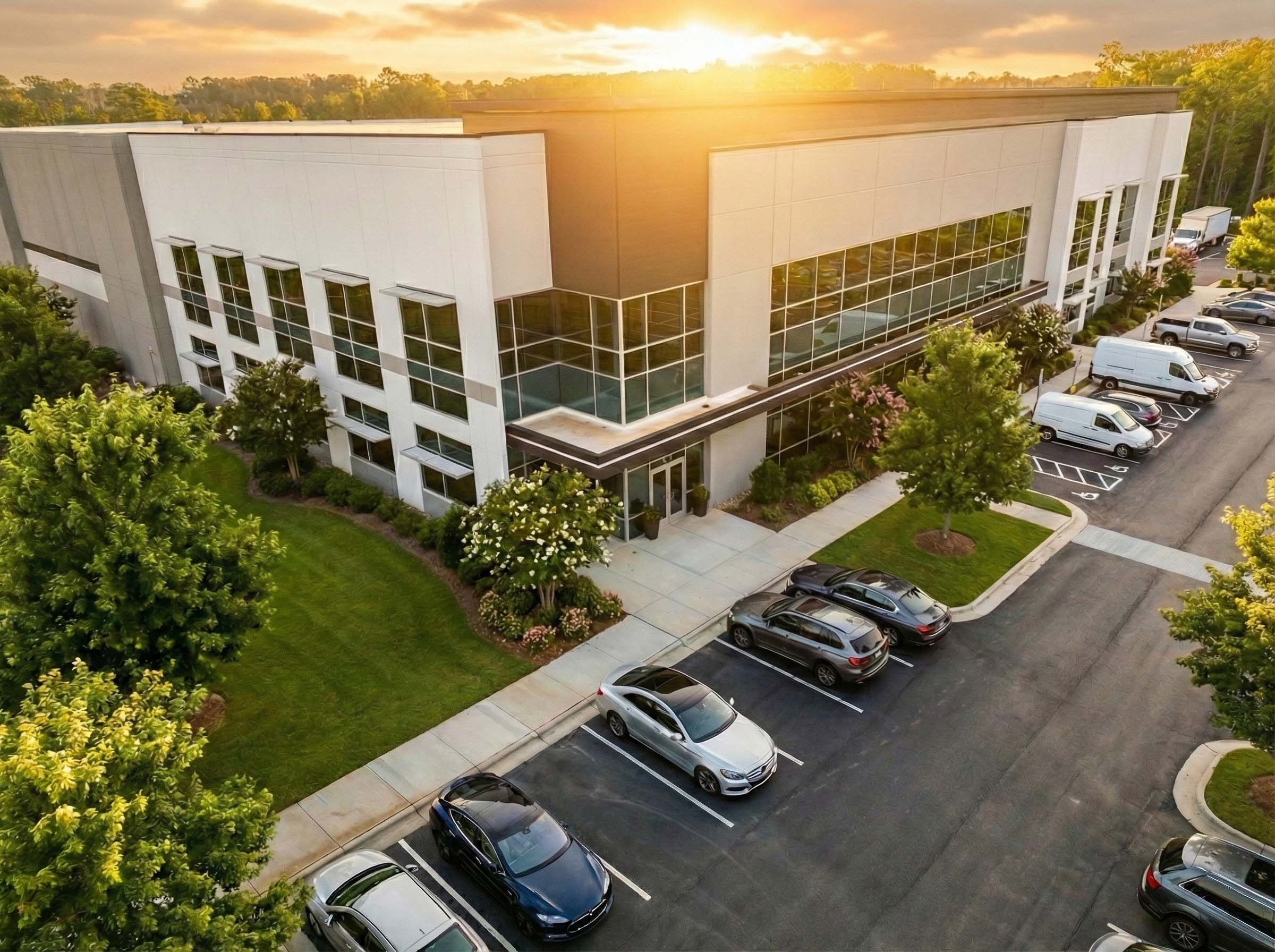 Aerial view of office building entrance with parking lot at sunrise.