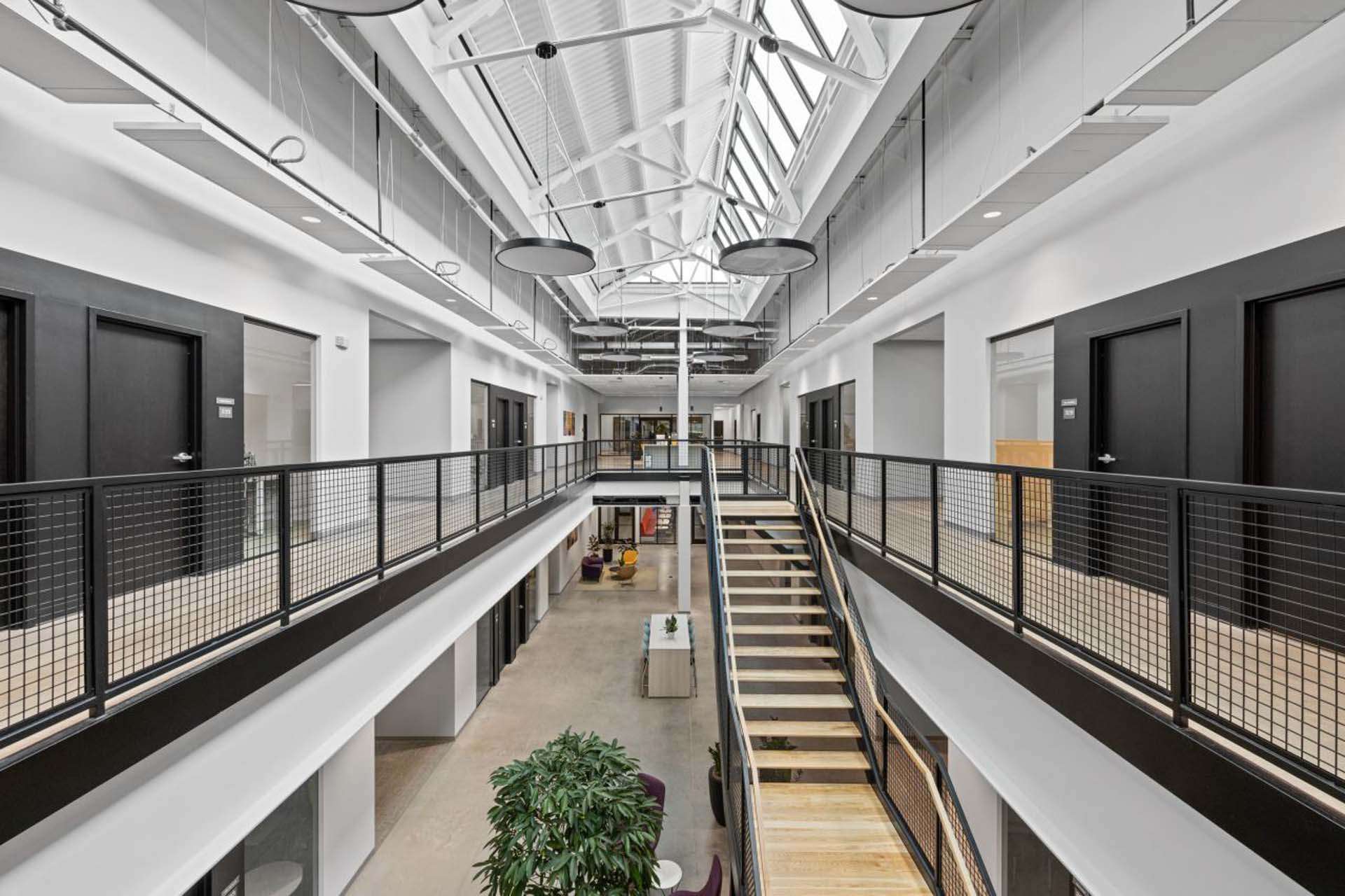 Two-story office atrium with a skylight, wood staircase, and mesh-panel railings.
