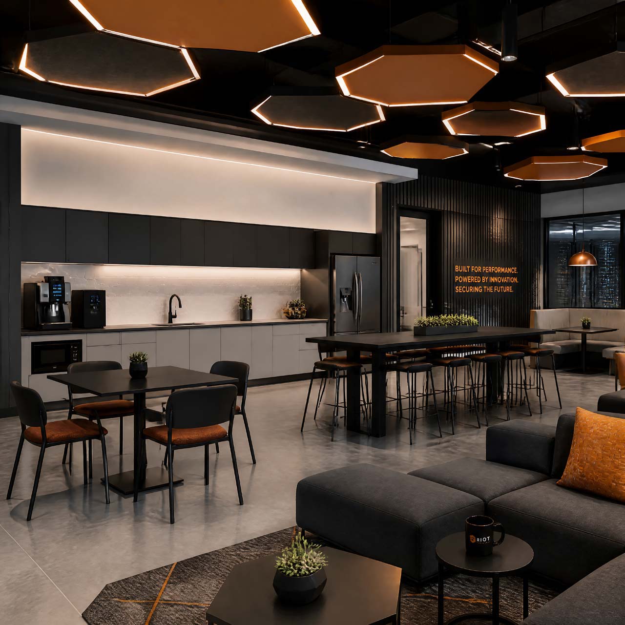 Office breakroom with hexagonal pendant lighting, kitchen area, and lounge seating with a wall graphic reading 