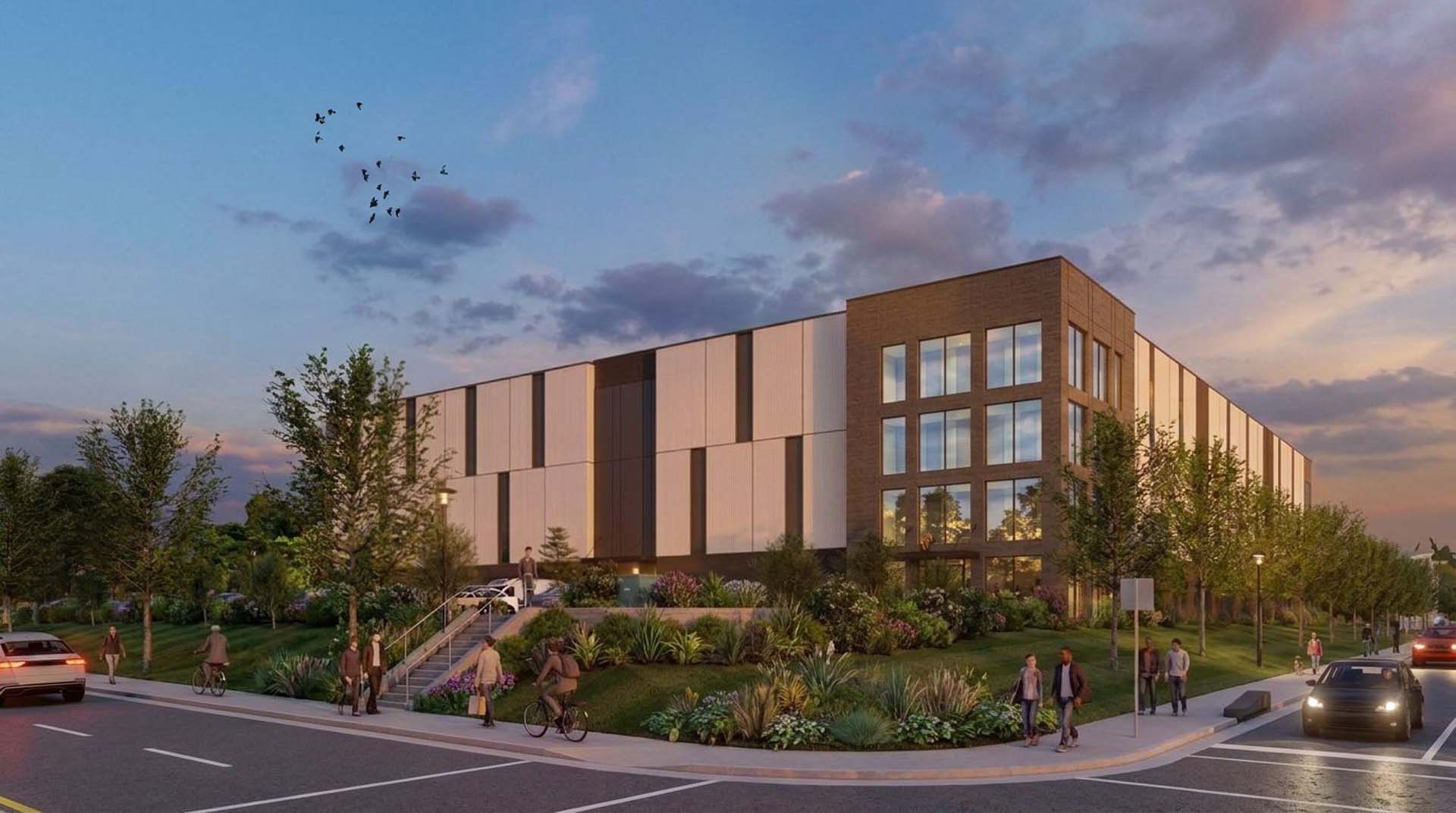 Exterior of self storage building at dusk with lit windows, concrete panel entrance, and street landscaping.