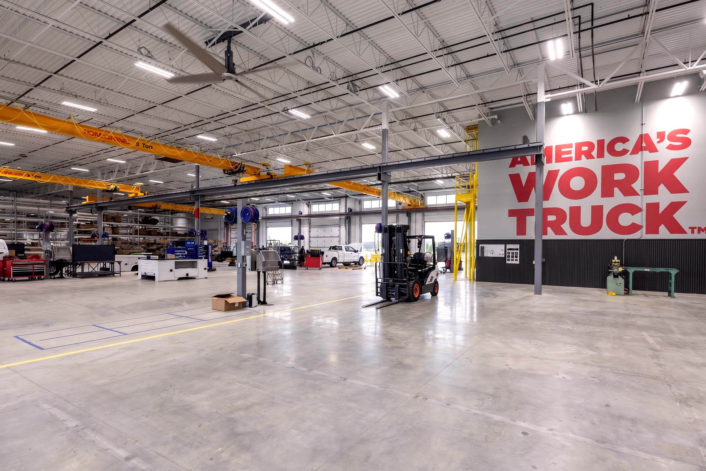 Interior of an industrial truck equipment facility with a forklift, overhead cranes, and workstations.